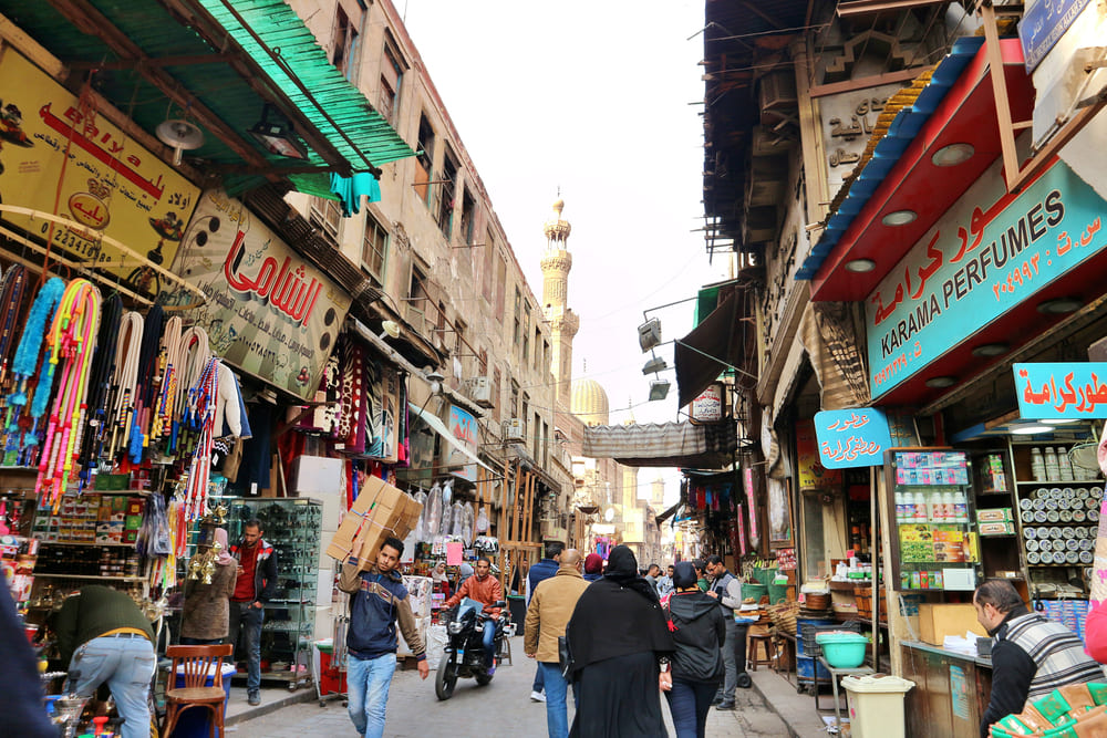 Cairo, Egypt. Busy streets in Khan el Khalili bazar shops store fronts mosque minaret people working walking by souvenirs